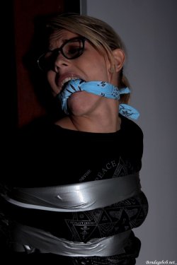Model Chloe Toy wearing glasses jeans and a t shirt tied up with tape bound to a pole and gagged with a knotted bandanna 