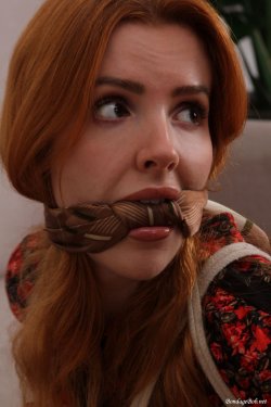 A close up of Scarlett Jones gagged with a knotted scraf cleave gag looking back over her shoulder her eyes wide with fear